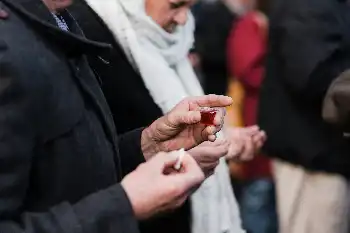 A person holding a communion bread piece and a small communion cup during a church service.